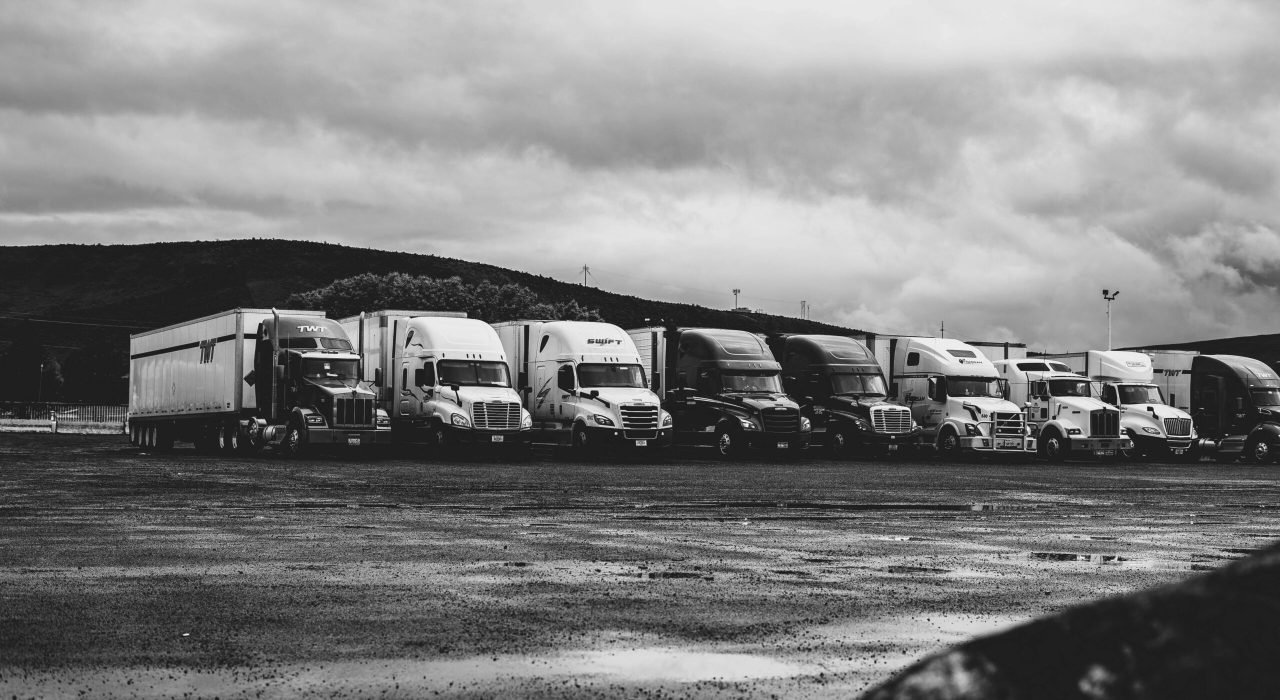 Row of parked semi trucks in a rainy lot, captured in a dramatic black and white setting.